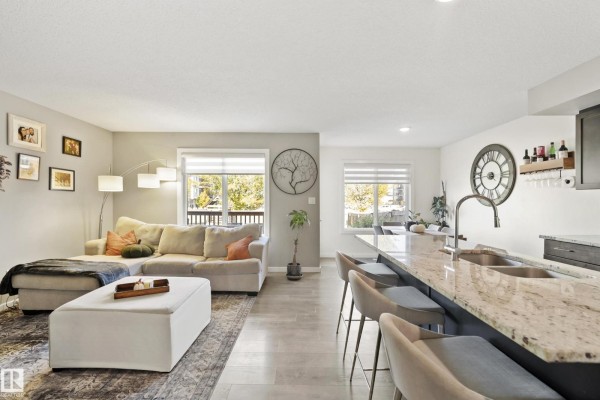 Living room with a sectional sofa, ottoman, and large area rug facing a window with blinds. - 6520 59 Av, Beaumont