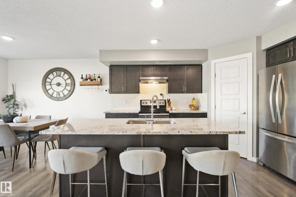 Kitchen island with granite countertop and bar stools, next to dark cabinets, stainless steel refrigerator, and dining table. - 6520 59 Av, Beaumont