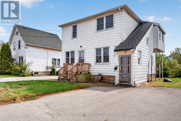 Side exterior view of a white two-story house showing the driveway and adjacent properties. - 6520 Barker Street, Niagara Falls