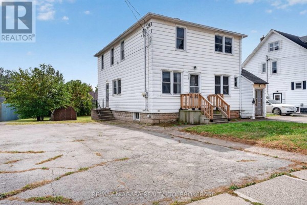 Side view of a white two-story house with a weathered attached structure and wood siding. - 6520 Barker Street, Niagara Falls