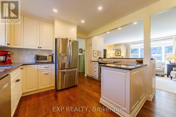 Kitchen with cream cabinets, granite countertops, stainless steel appliances, and hardwood floors, open to a living area. - 6530 Bunker Road, Ottawa