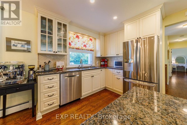 Kitchen with cream cabinets, granite countertops, stainless steel appliances, and a window with floral blinds. - 6530 Bunker Road, Ottawa