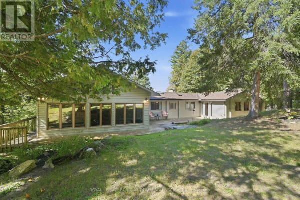 Aerial view of a house nestled among pine trees, with a large deck, situated on the edge of a dark lake with surrounding forest. - 654 A Chimo Road S, Greater Madawaska