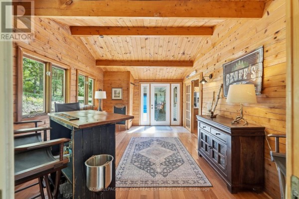View of a calm lake surrounded by evergreen trees, with two green Adirondack chairs and a fire pit in the foreground. - 654 A Chimo Road S, Greater Madawaska