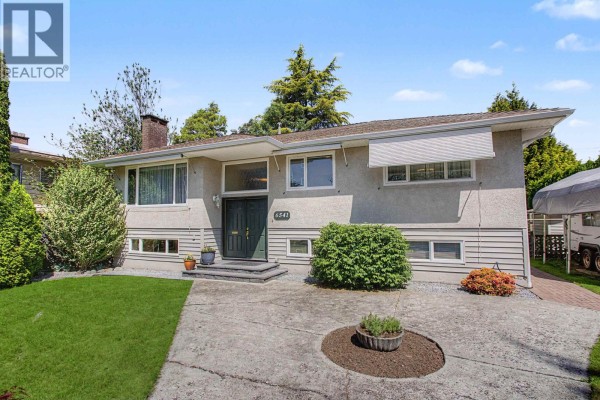 Front exterior view of the stucco house with a concrete driveway and manicured bushes. - 6541 Grant Street, Burnaby
