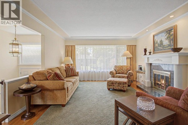 Living room with a patterned armchair, ottoman, two lamps, and a fireplace with marble surround. - 6541 Grant Street, Burnaby
