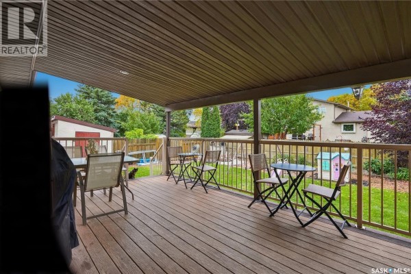 View from a covered wooden deck overlooking a grassy backyard with a play structure. - 6546 Rush Place, Regina