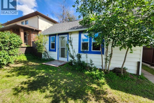 Front corner view of a white house with blue trim, surrounded by grass and trees. - 655 3 Avenue W, Drumheller