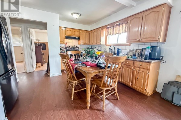 Kitchen with wooden cabinets, laminate flooring, a wooden dining table with four chairs, and a stainless steel refrigerator. - 655 Queen St W, Sault Ste  Marie