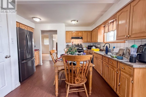 Kitchen with wooden cabinets, laminate flooring, a wooden dining table with four chairs, and a stainless steel refrigerator. - 655 Queen St W, Sault Ste  Marie