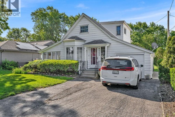 Exterior of a white house with green lawn, hedges, and a parked car. - 6565 Riverside Drive East, Windsor