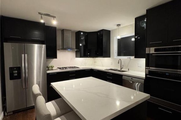 Modern kitchen with black high-gloss cabinets, a stainless steel refrigerator, white countertops, and an island with seating. - 657 Jupiter Court, Sudbury