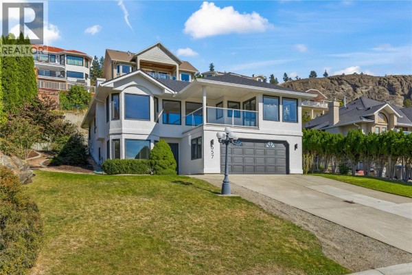 Front view of the house at 657 Royal View Drive with a sloping green lawn and trees. - 657 Royal View Drive, Kelowna