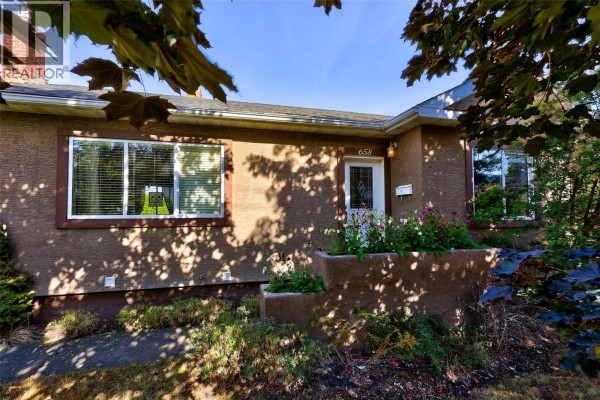 Front exterior of a brown stucco house with a white door, window boxes, and landscaping. - 658 Dominion Street, Kamloops