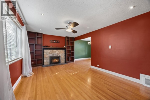Living room with red walls, hardwood floors, stone fireplace, built-in bookshelves, and ceiling fan. - 658 Dominion Street, Kamloops