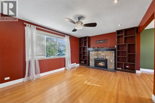 Living room with red walls, hardwood floors, stone fireplace, built-in bookshelves, and white curtains. - 658 Dominion Street, Kamloops