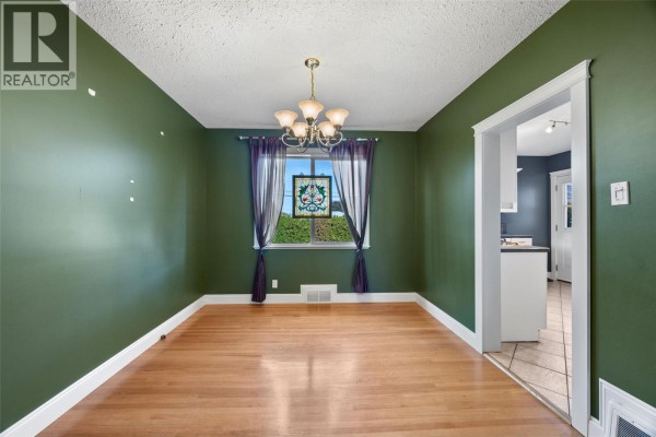 Dining room with dark green walls, hardwood floors, chandelier, and a window with stained glass. - 658 Dominion Street, Kamloops