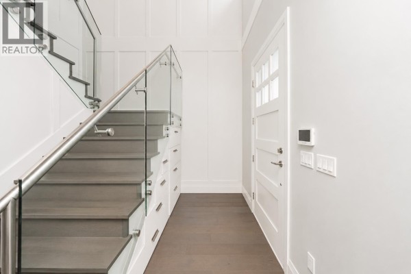 Interior hallway with dark wood floors, white walls, a staircase with glass railing, and built-in cabinets. - 6585 Halifax Street, Burnaby