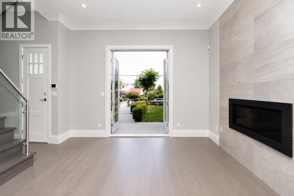 Living room with light gray walls, a modern gas fireplace, and double doors opening to a backyard. - 6585 Halifax Street, Burnaby