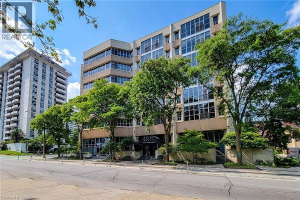 Street view of a modern brick and glass apartment building with surrounding trees. - 66 Bay Street S Unit# 414, Hamilton