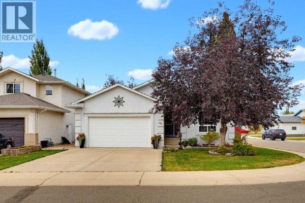 Front exterior of a two-story house with a white garage door and dark red tree. - 66 Dumas Crescent, Red Deer