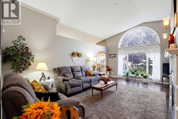 Living room with vaulted ceilings, a large arched window, two sofas, and a coffee table. - 66 Dumas Crescent, Red Deer