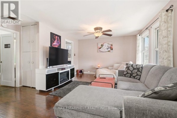 Living room with a large sectional sofa, TV, and hardwood floors. - 66 East 32nd Street, Hamilton