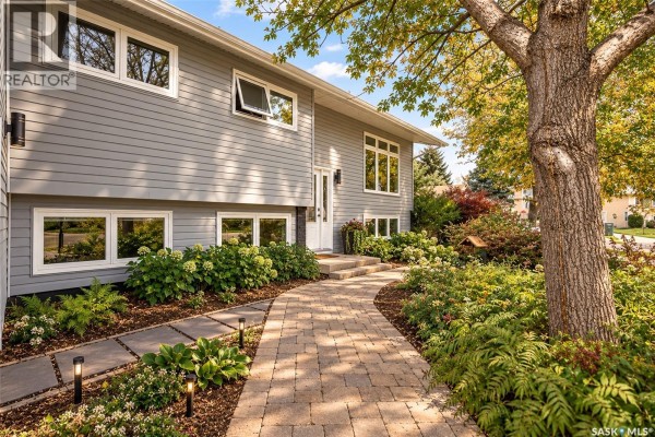 Paved walkway leads to the front entrance surrounded by green landscaping and flowering shrubs. - 66 Edelweiss Crescent, Moose Jaw