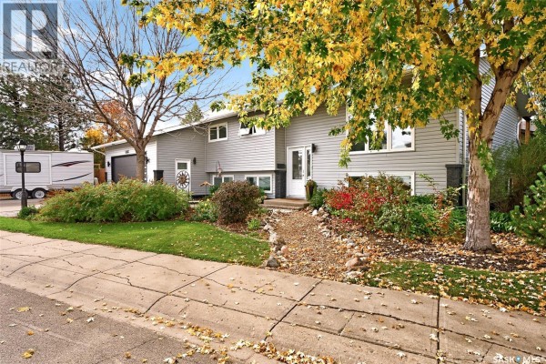 View of the property from the street showing the house, driveway, landscaping, and mature trees. - 66 Edelweiss Crescent, Moose Jaw