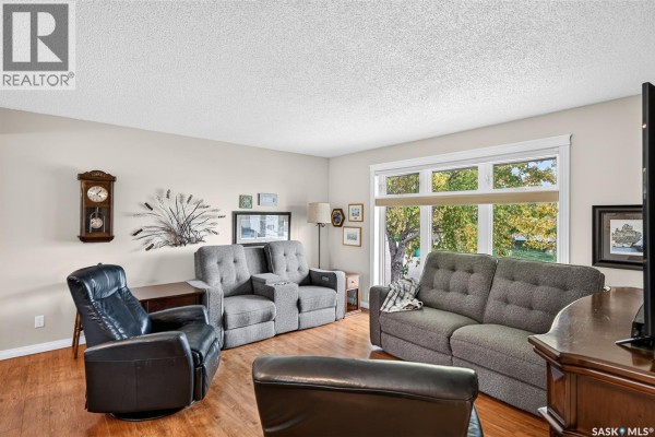 Living room with gray upholstered couches and a black leather recliner, wood laminate flooring. - 66 Edelweiss Crescent, Moose Jaw