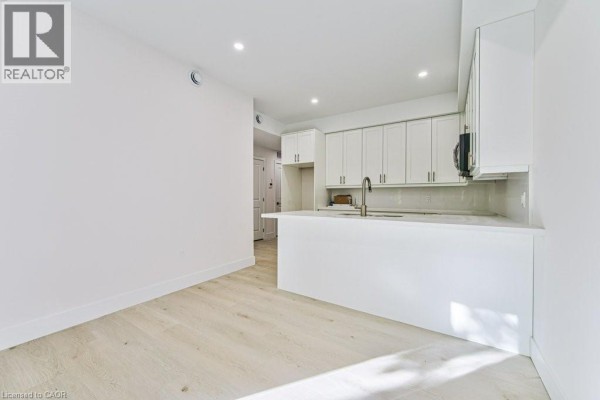 Open concept living area with a white kitchen island and light wood laminate flooring. - 66 Gage Avenue Unit# 1, Kitchener