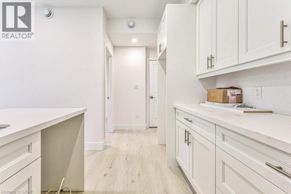View down a hallway from the kitchen, showing white cabinets and light wood floors. - 66 Gage Avenue Unit# 1, Kitchener