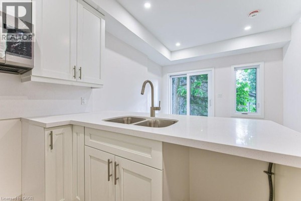 Close-up of the kitchen sink and island, with white cabinets and quartz countertops visible. - 66 Gage Avenue Unit# 1, Kitchener