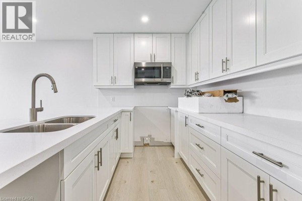 U-shaped kitchen with white cabinets, quartz countertops, stainless steel microwave, and light wood flooring. - 66 Gage Avenue Unit# 2, Kitchener