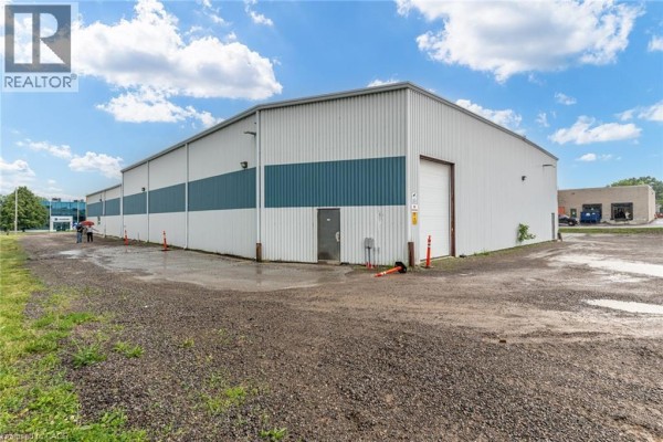 Rear view of the commercial building showing a large bay door, access door, and surrounding gravel lot. - 66 Innovation Drive, Dundas