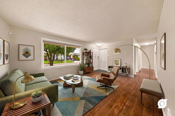 Living room with green sofa, leather armchair, wooden floors, and a large window overlooking the street. - 66 Meighen Bay, Winnipeg