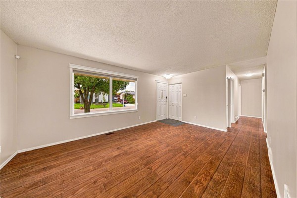Empty living room with wooden floors, a large window, and hallway leading to other rooms. - 66 Meighen Bay, Winnipeg