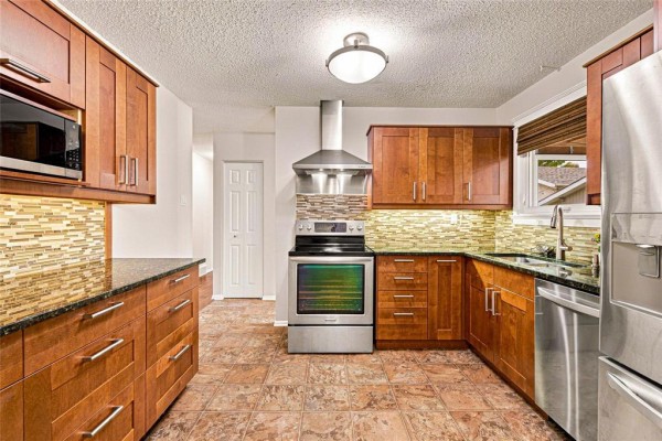 Kitchen with wooden cabinets, granite countertops, stainless steel appliances, and mosaic tile backsplash. - 66 Meighen Bay, Winnipeg