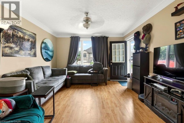 Living room with a large grey sectional sofa, beige walls, wood floors, and a dark front door. - 66 Queen Street S Unit# Front Unit, Thorold