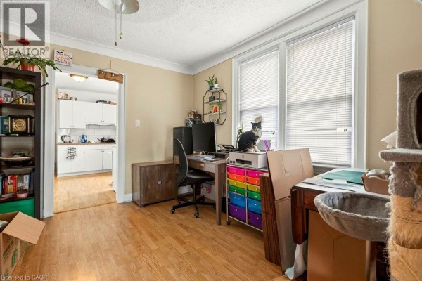 Room with a desk, computer monitors, a cat, and a view into a white kitchen. - 66 Queen Street S Unit# Front Unit, Thorold