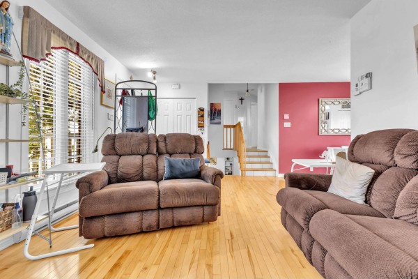 Living room featuring brown sofas, hardwood floors, white walls, and a view of the staircase. - 66 Rue Paquette, Gatineau