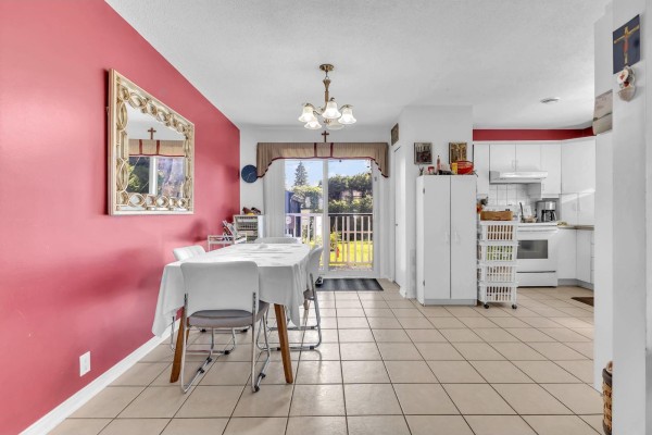 Dining area with a white-covered table, pink accent wall, and an open-concept kitchen with white cabinets. - 66 Rue Paquette, Gatineau