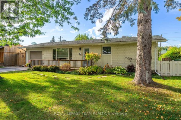 Front facade of a beige brick bungalow with a wooden deck and mature trees in the yard. - 66 Still Water Drive, Ottawa