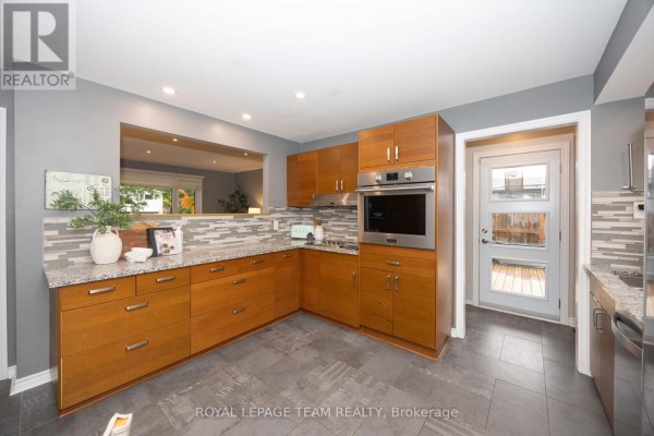Modern kitchen with wood cabinetry, granite countertops, stainless steel appliances, and a glass door to the exterior. - 66 Still Water Drive, Ottawa