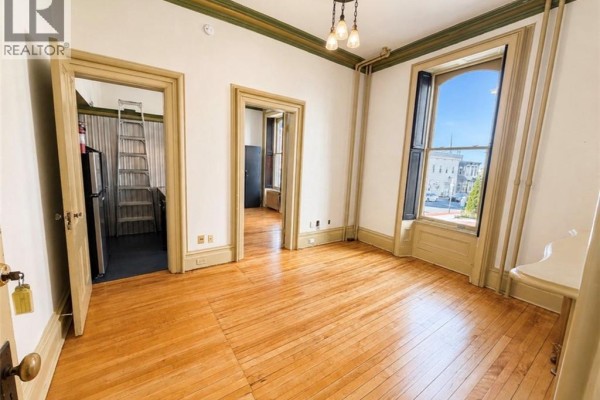 Interior room with wood floors, white walls, and an open doorway to the kitchen. - 66 Sydney Street Unit# 1, Saint John