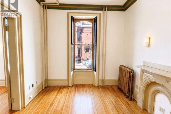 Room with wood floors, white walls, a bay window, and a decorative radiator. - 66 Sydney Street Unit# 1, Saint John