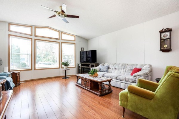 Living room with a large bay window, wood-look laminate flooring, and a gray sofa with decorative pillows. - 66 Village Drive, Ste Anne