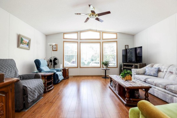 Wide shot of the living room featuring a bay window, a television, a sofa, and a green armchair. - 66 Village Drive, Ste Anne