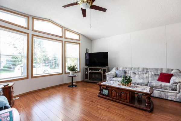 View of the living room with wood laminate flooring, a sofa, and a television on a media stand. - 66 Village Drive, Ste Anne