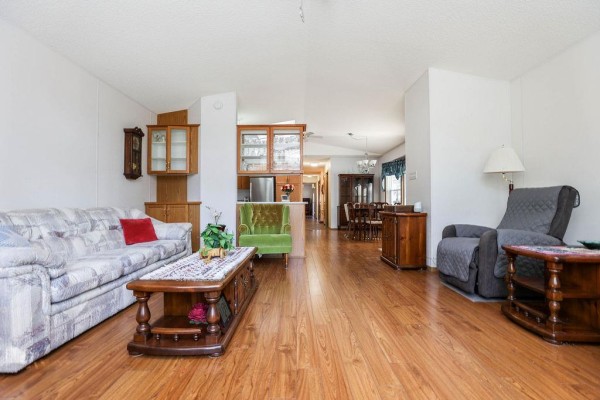 Living room and dining room with wood floors, a sofa, a green accent chair, and a dining table in the background. - 66 Village Drive, Ste Anne